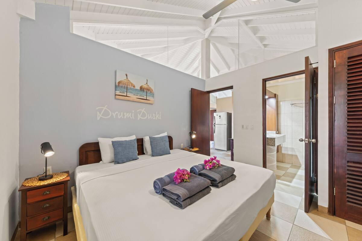 A bedroom with a large bed, a nightstand, a wall art piece, and a door leading to a bathroom.