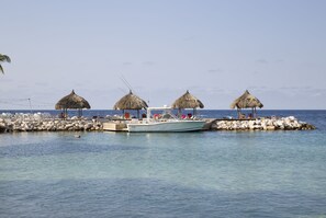 A boat docked at a pier with thatched-roof structures and a clear view of the sea. - Blue Bay Villas (Sint Michiel)