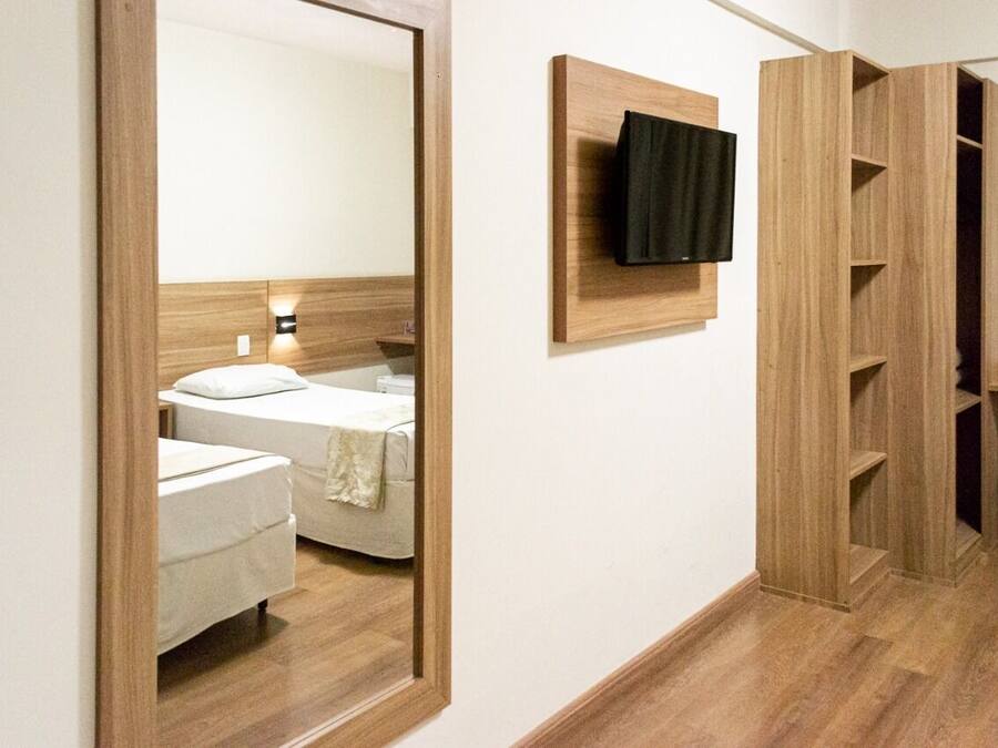 A hotel room with a wooden headboard, a bed with white linens, a mounted TV, and built-in wooden shelving.