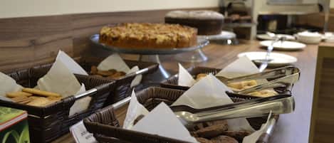 A buffet setup with various food items in wicker baskets, a cake on a stand, and a coffee machine in the background.