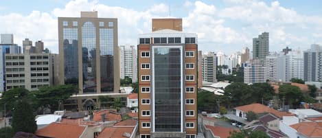 Un edificio de gran altura con fachada de vidrio moderna, rodeado de edificios residenciales con tejados de tejas rojas.