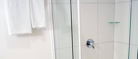A glass-enclosed shower with a white tiled floor and a towel rack with folded towels.