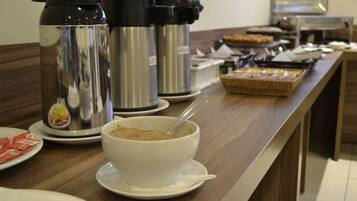 A buffet setup with a bowl of cereal, coffee makers, and a variety of food items on a counter.