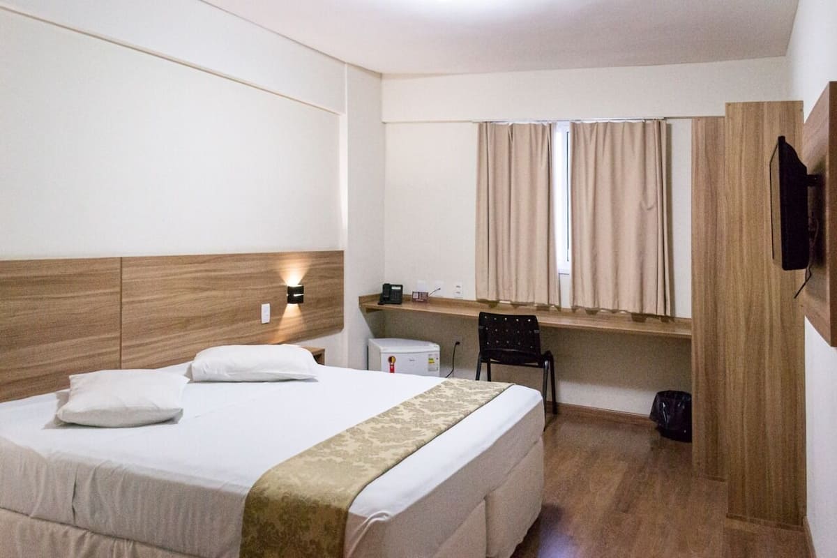 A hotel room with a bed, a desk, a chair, a television, and a window with curtains.