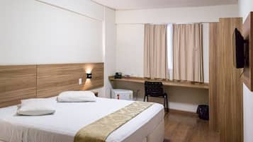 Une chambre d’hôtel avec un lit, un bureau, une chaise, une télévision et une fenêtre avec des rideaux.