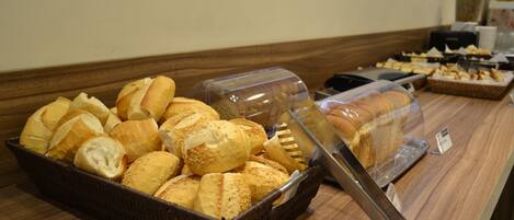 A buffet counter with various breads and pastries, including croissants and baguettes, displayed in baskets and covered containers.