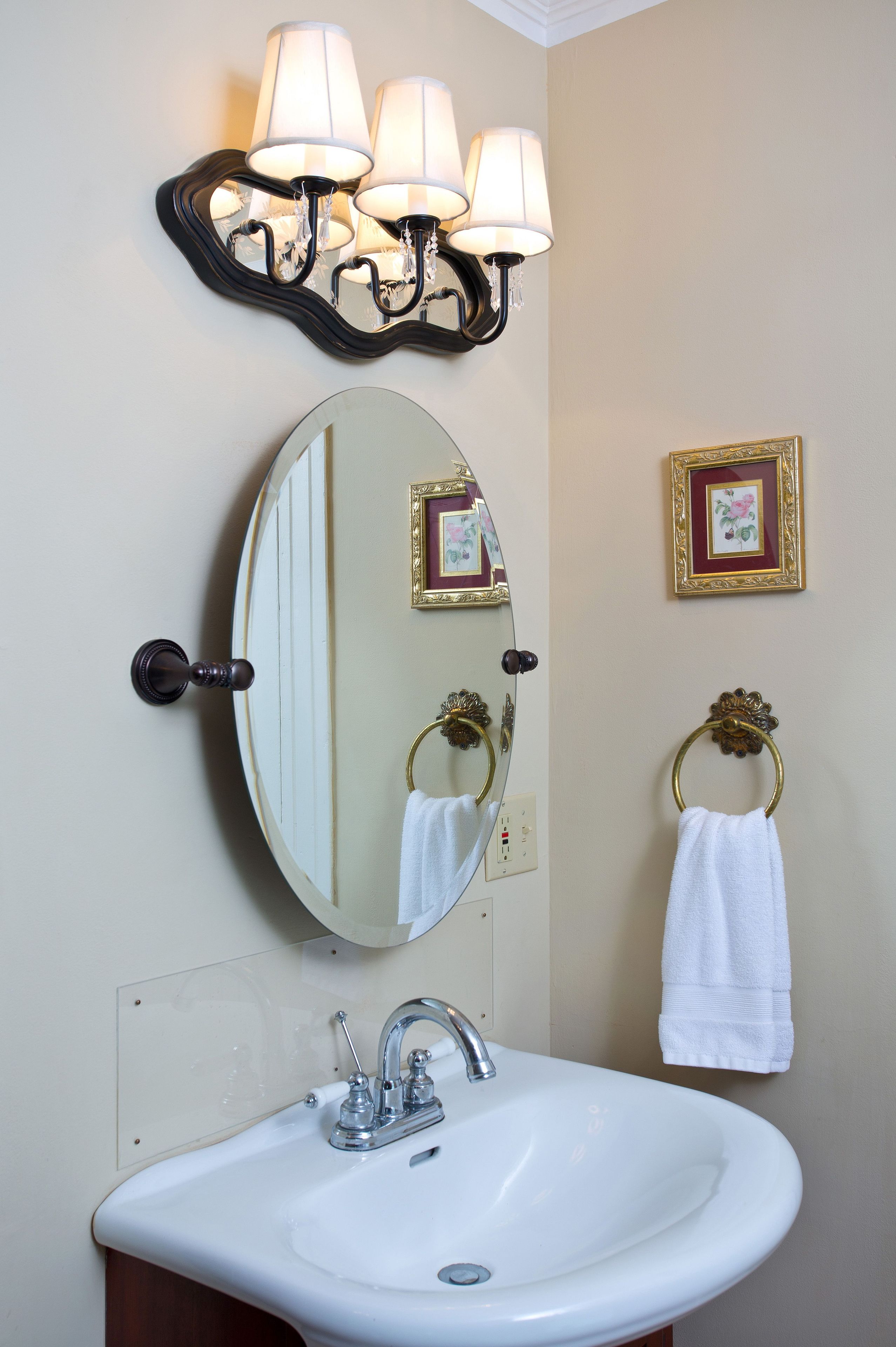 Un baño con lavamanos blanco, un espejo, un aplique en la pared y dos cuadros enmarcados.