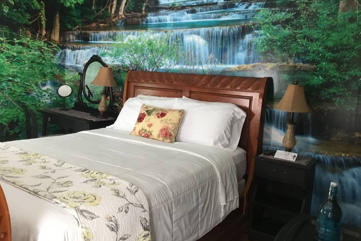 A bedroom with a bed, a nightstand, a lamp, and a wall mural of a waterfall.