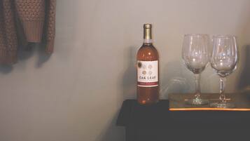 A bottle of Oak Leaf wine and two glasses on a table against a wall with a framed picture.