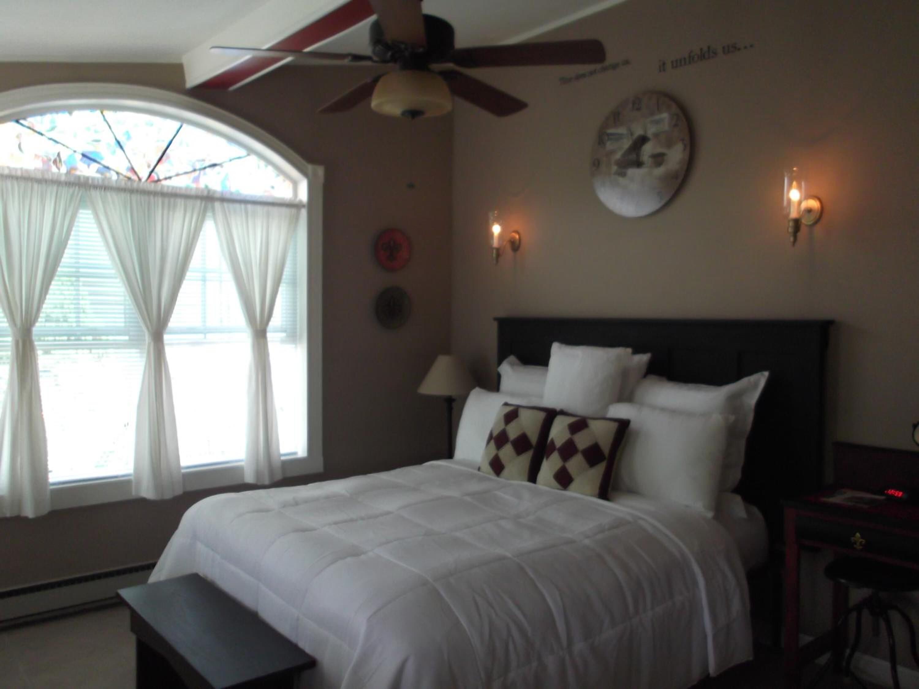 Quarto com cama, ventoinha no teto, relógio e janela com cortinas.