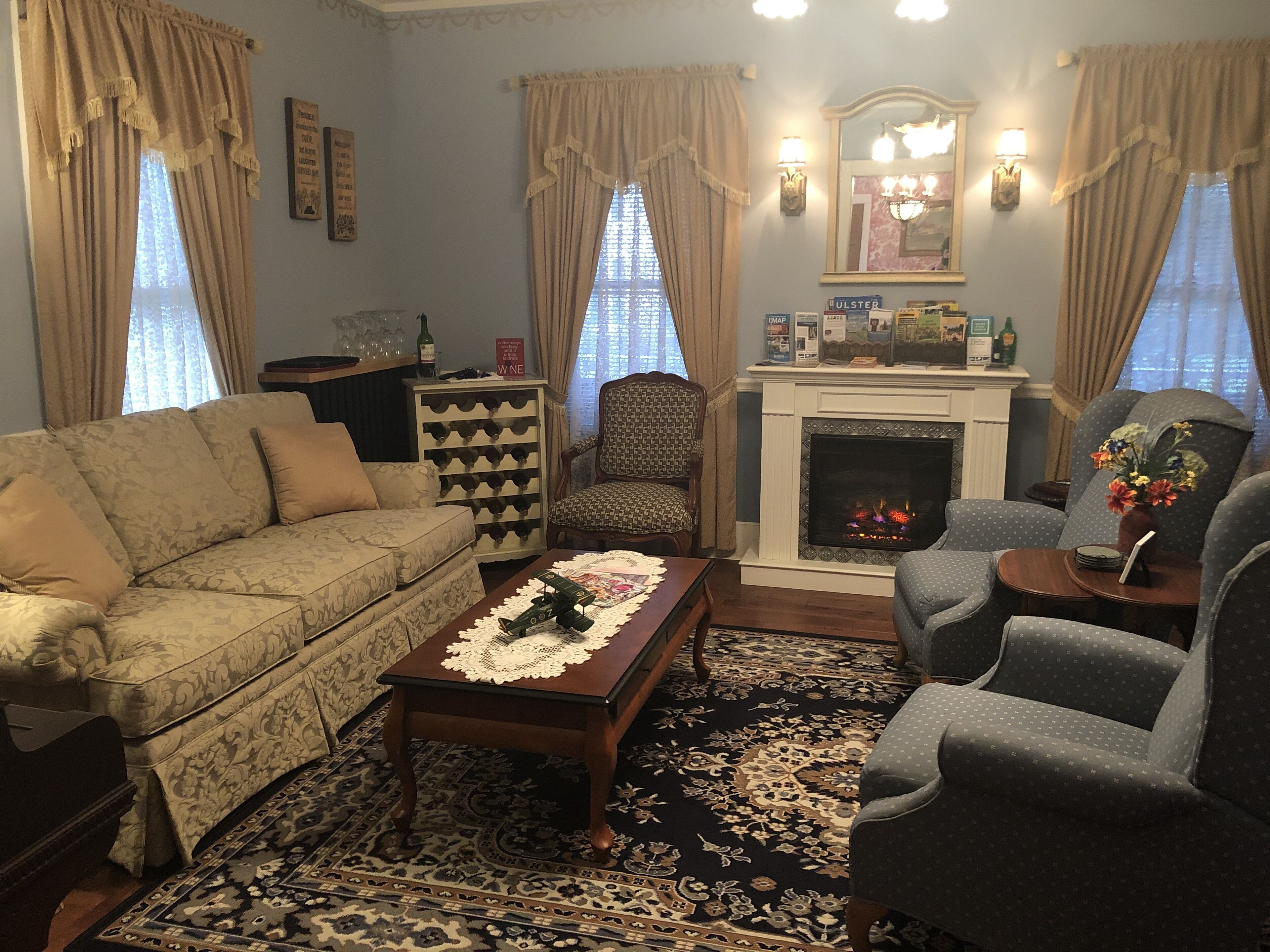 A living room with a sofa, armchairs, a coffee table, a fireplace, and a wine rack.