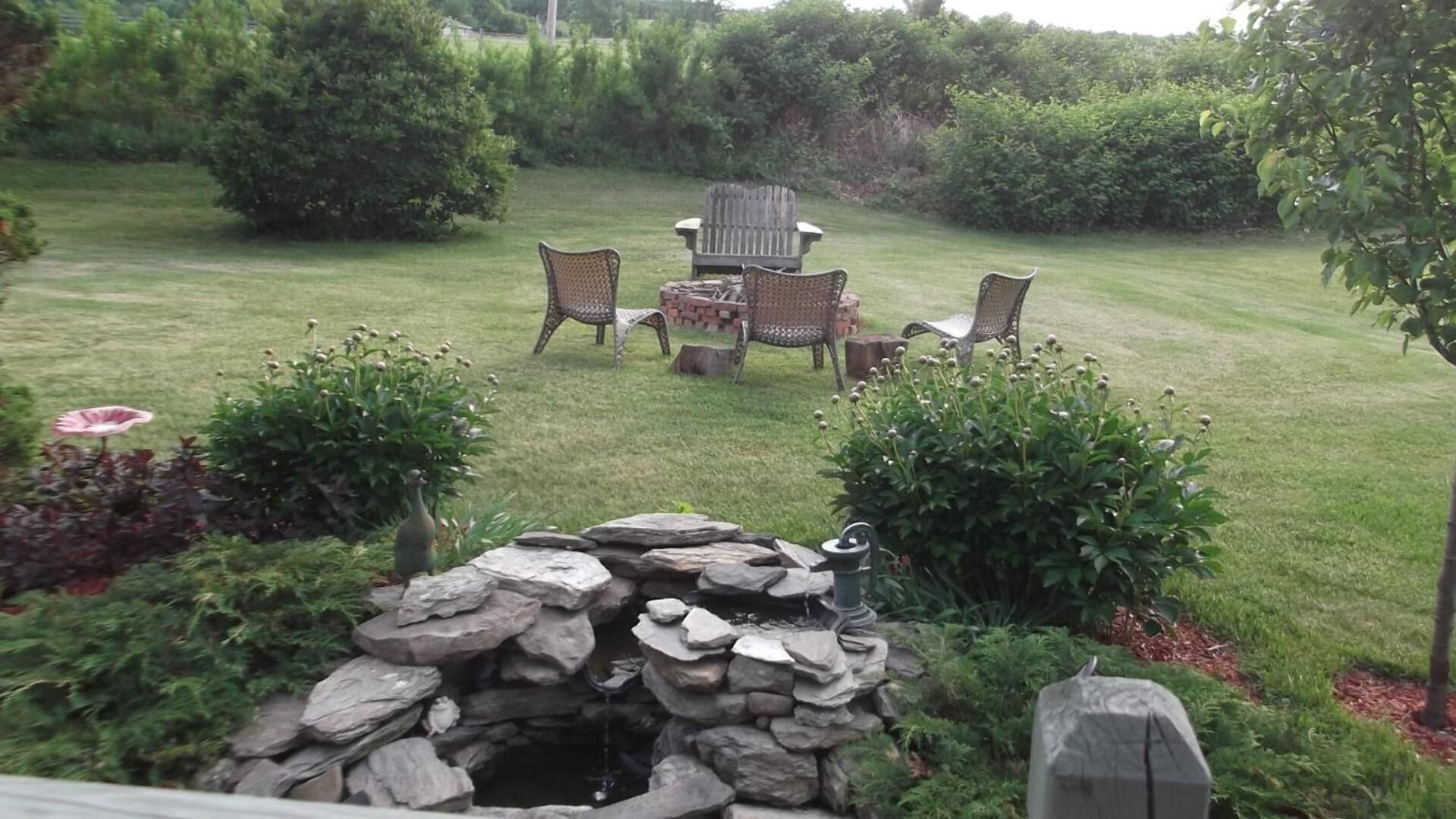 A backyard with a stone fountain, a wooden deck, and outdoor furniture.