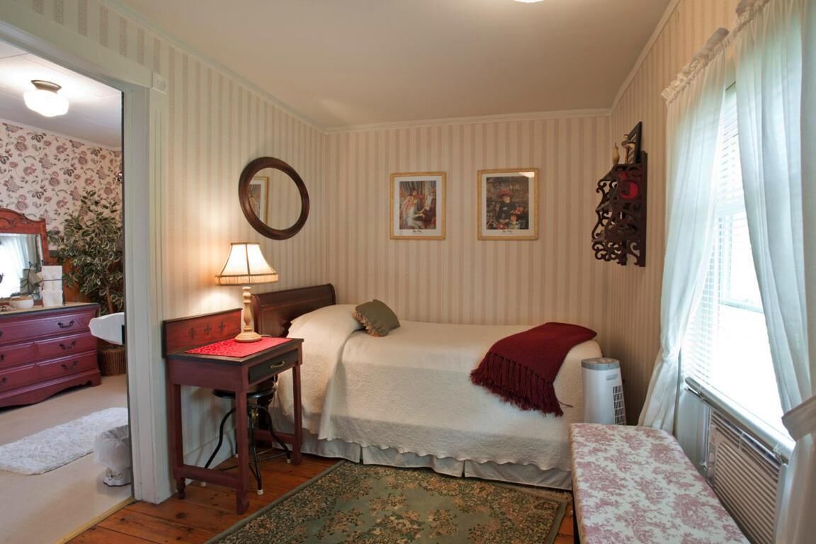A bedroom with a bed, a desk, a chair, a mirror, and a radiator.