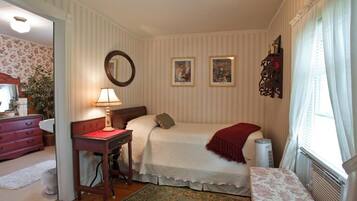 A bedroom with a bed, a desk, a chair, a mirror, and a radiator.