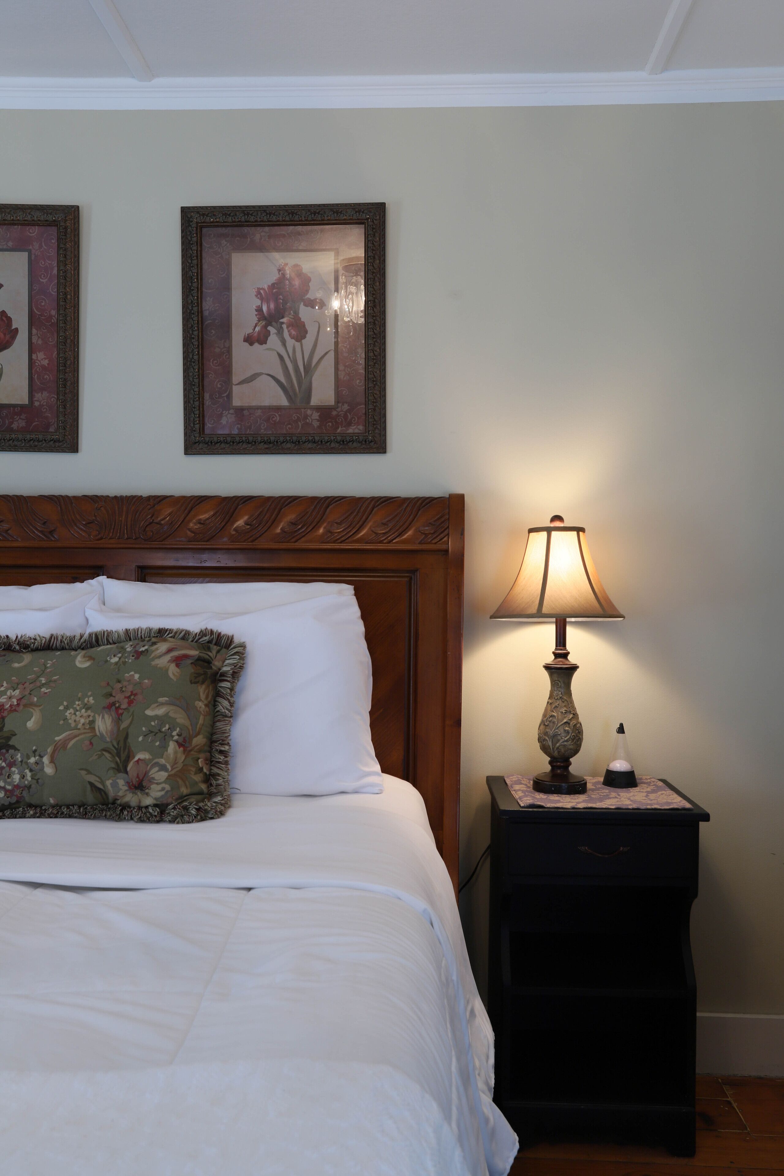 A neatly made bed with a floral pillow, a wooden headboard, and a nightstand with a lamp.