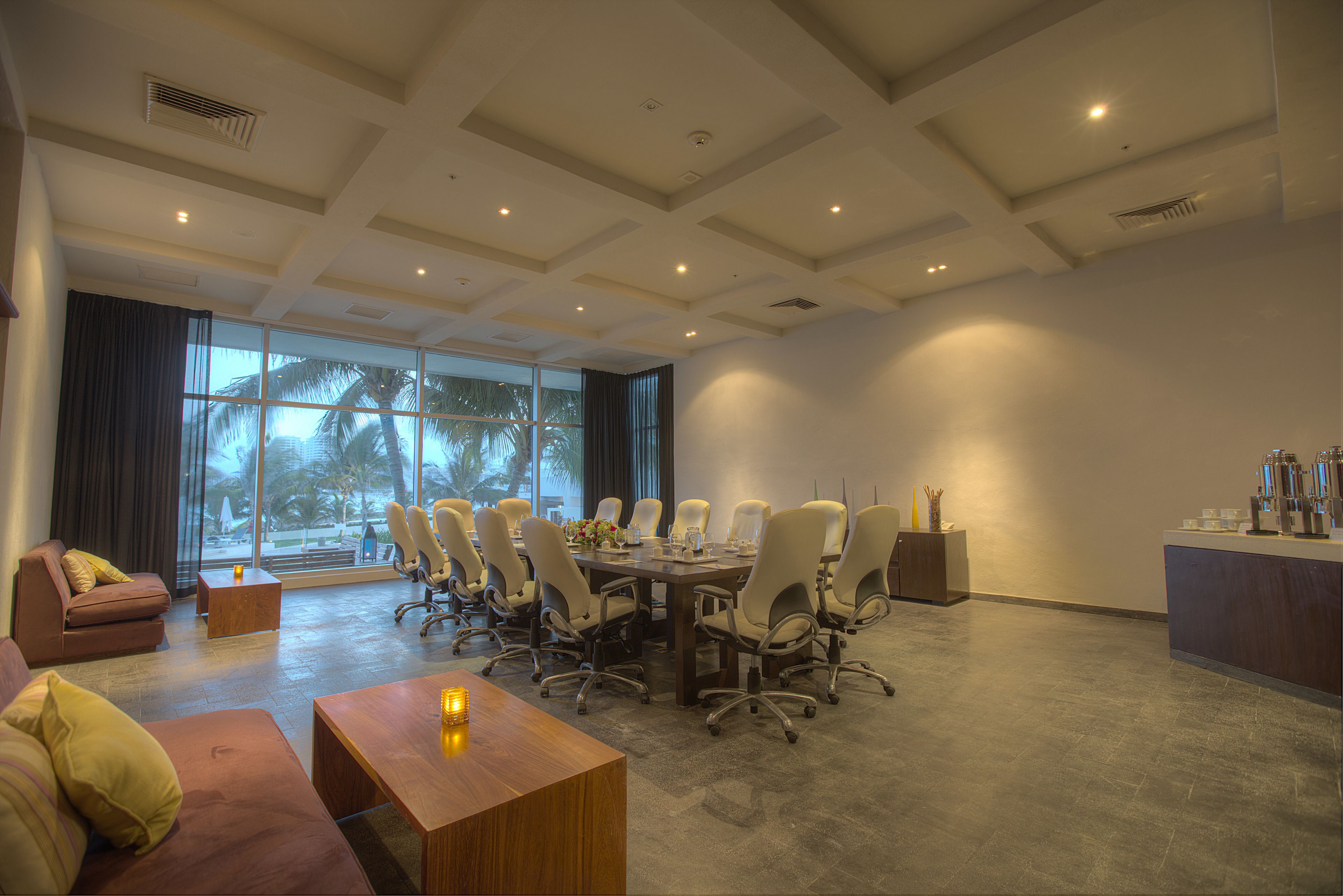 Una amplia sala de conferencias con una gran mesa, asientos cómodos y vistas a palmeras a través de grandes ventanales.