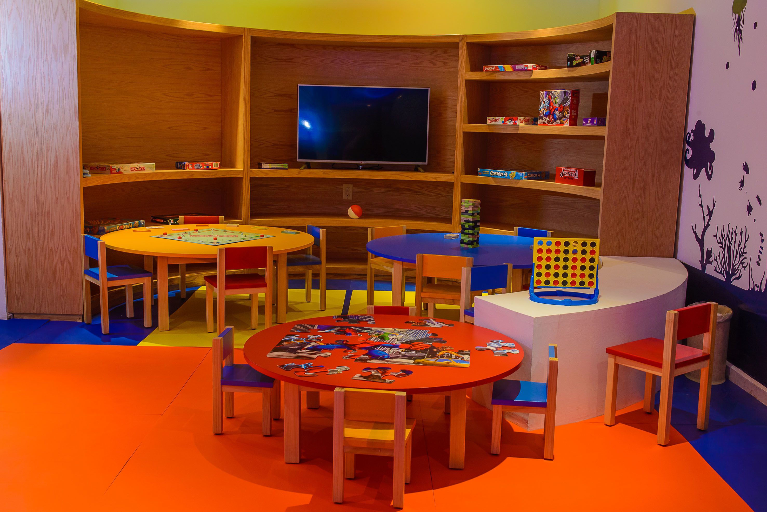Espaço infantil com televisão, estantes de livros e uma mesa com cadeiras.