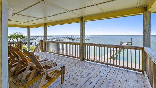 A wooden deck with chairs overlooking a beach and pier. -  Copano Bay Sunset - LOCATION! LOCATION! LOCATION!!! (Rockport)