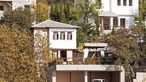 Un borgo collinare con edifici in pietra tradizionali, un'auto parcheggiata di fronte e montagne sullo sfondo.