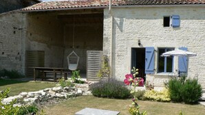 A rustic stone building with a tiled roof, a hanging chair, a bench, and a small table in the garden. - Cosy, pet friendly cottage for 2 in pretty countryside (Crézières)