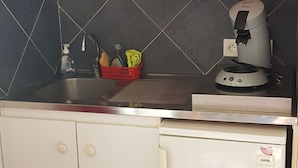 A compact kitchen with a refrigerator, a coffee maker, and a shelf with dishes and cups. - Studio in quiet garden  (Vieillevigne)