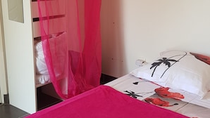 A room with a bed covered in a bright pink blanket, a white wardrobe with a mirror, and a red mosquito net over the wardrobe. - Studio in quiet garden  (Vieillevigne)