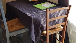 A dining area with a table set for two, a bookshelf, and a wall-mounted telephone. - Studio in quiet garden  (Vieillevigne)