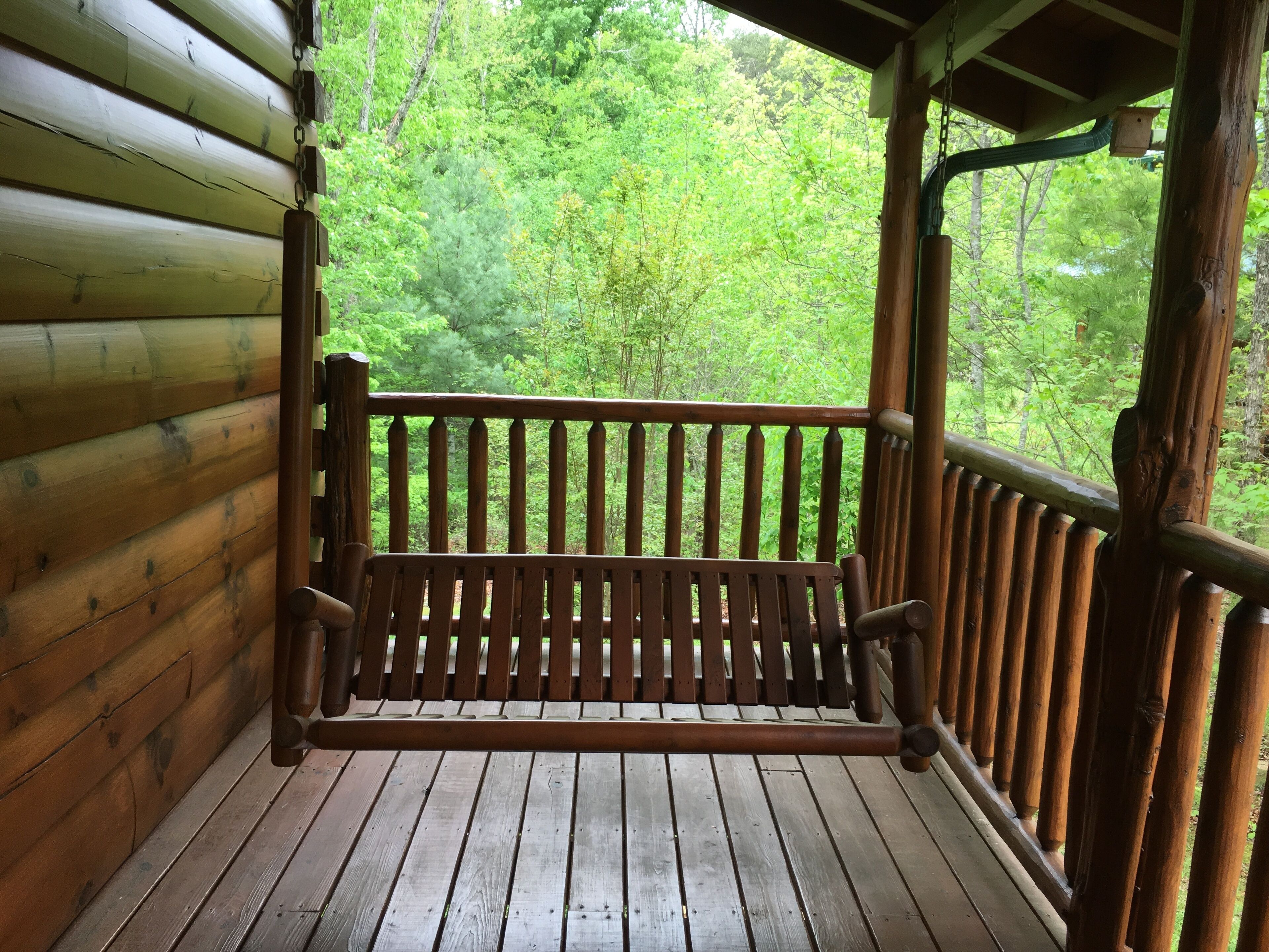 Eine Holzterrasse mit einer Bank, umgeben von einer Holzhütte und einem bewaldeten Hintergrund.