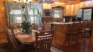 A wooden cabin-style kitchen with a dining area, featuring a wooden table, chairs, a microwave, and a refrigerator. - Luxury Cabin, 4 BD/4BA Suites,Half Bath, Game RM, Media RM, Fireplaces, Hot Tub (Sevierville)
