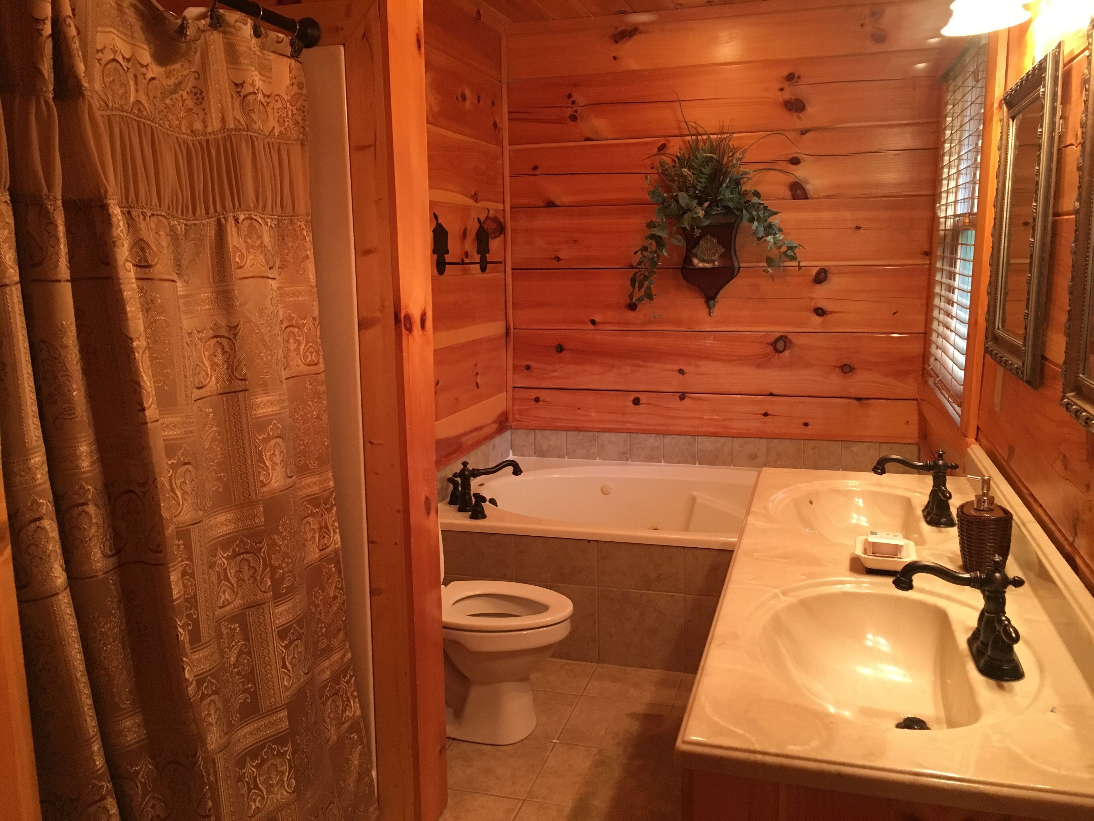 Une salle de bain aux murs lambrissés, équipée d’une baignoire, de toilettes et de deux lavabos.