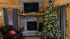 A cozy living room with a stone fireplace, a Christmas tree, and a leather armchair. - Luxury Cabin, 4 BD/4BA Suites,Half Bath, Game RM, Media RM, Fireplaces, Hot Tub (Sevierville)