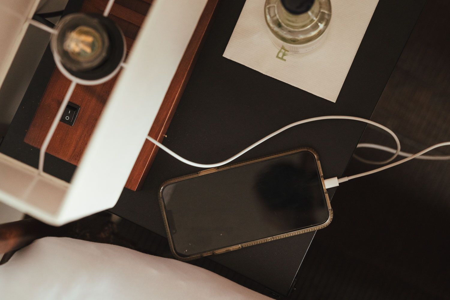 A smartphone charging on a table with a wooden surface and a white cushion.