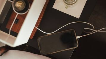 A smartphone charging on a table with a wooden surface and a white cushion.