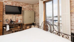 A bedroom with a brick wall, a bed, a television, a cabinet, and a window with a view of the sea. - Rocksalt (Folkestone)