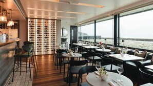A restaurant with a wine rack, tables, chairs, and a view of the beach. - Rocksalt (Folkestone)