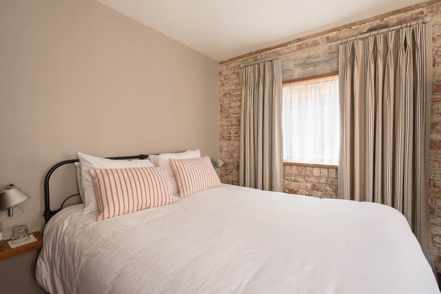 A bedroom with a large bed, a brick wall, and a window with curtains.