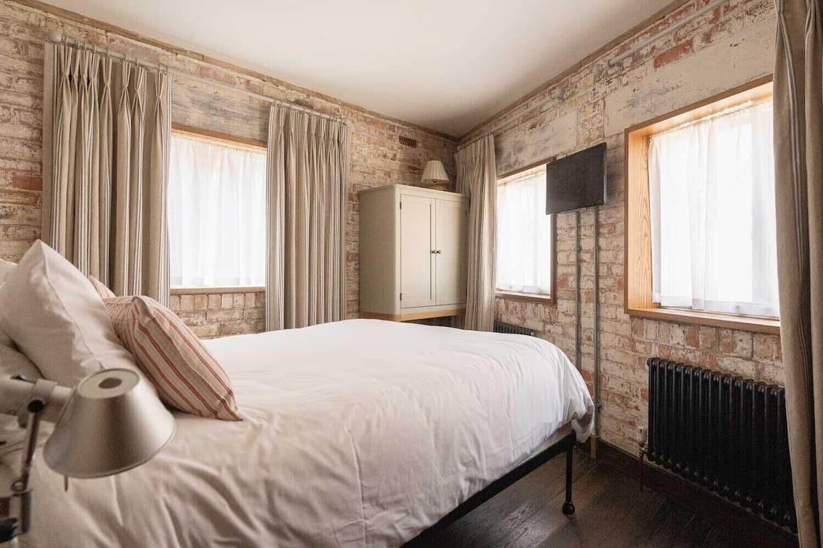 A bedroom with a bed, curtains, a radiator, and a TV.