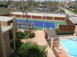 A tennis court with a pool and palm trees.