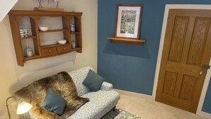 A room with a patterned sofa, a wooden cabinet with dishes, a framed picture, and a door. - Braemore Walled Garden B&B (Garve)