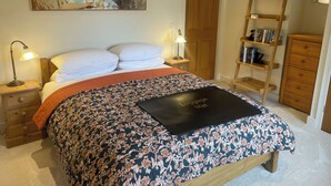 A bedroom with a bed, a nightstand, a bedside lamp, a wooden ladder, a bookshelf, and a door. - Braemore Walled Garden B&B (Garve)