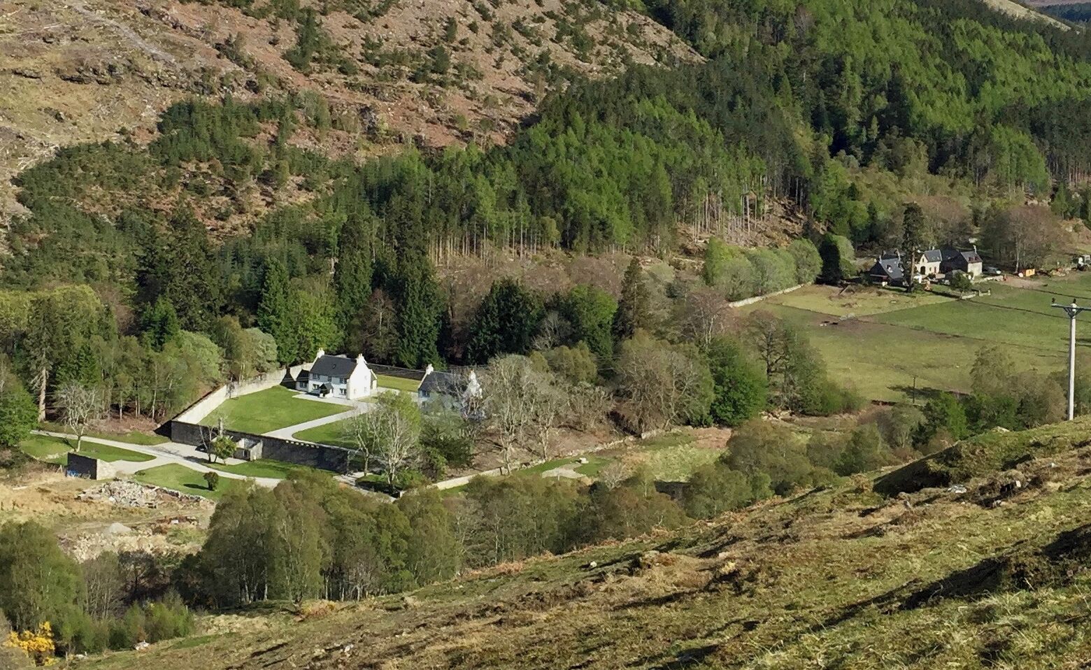 A rural landscape with a white house surrounded by trees and fields.