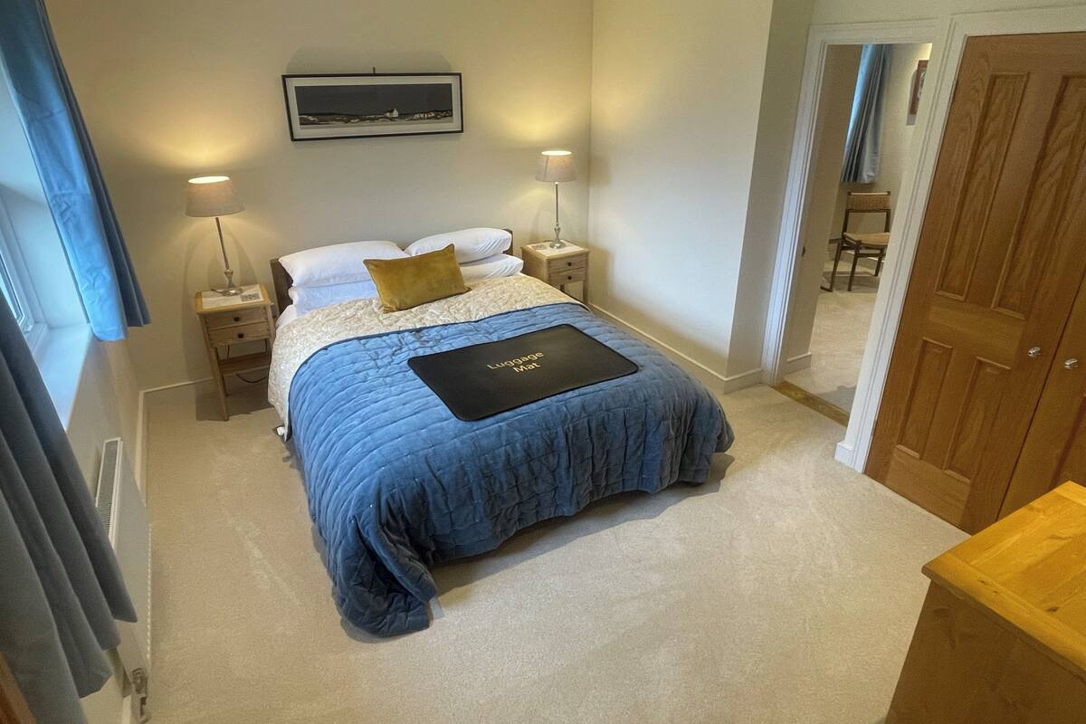 Une chambre à coucher avec un lit, des lampes de chevet, un tableau encadré au mur et un tapis à bagages sur le lit.