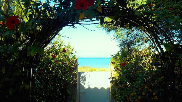 An arched doorway leading to a beach with a clear view of the sea.