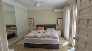A bedroom with a bed, a ceiling fan, an air conditioning unit, and a door with a patterned curtain.