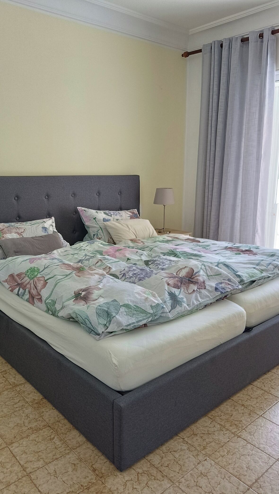 Un letto con copriletto floreale, una testiera grigia e una lampada da comodino.