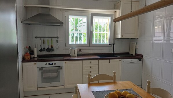 Cocina con alacenas blancas, estufa, pileta y ventana con vista a follaje.