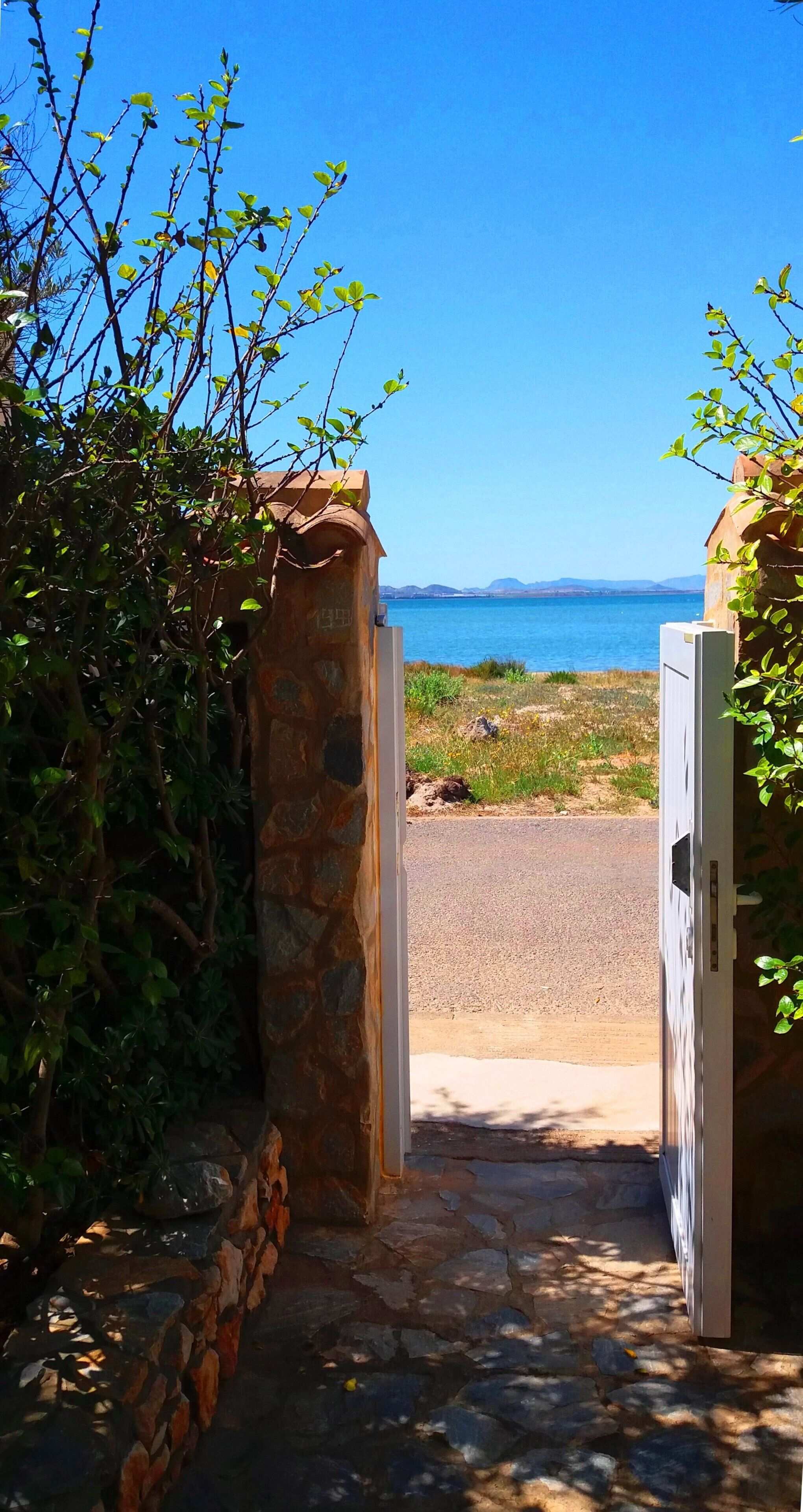 A stone archway leading to a paved path with a view of a body of water and distant mountains.