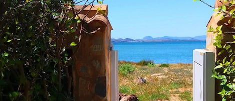 A stone archway leading to a paved path with a view of a body of water and distant mountains.