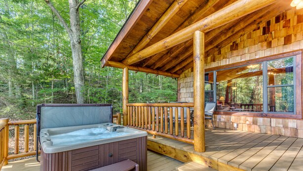 Terraza de madera con jacuzzi, baranda de madera y zona de estar cubierta con vista al bosque.