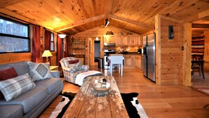 Interior acogedor de una cabaña con techo de madera, un sofá, una mesa de comedor y una zona de cocina.